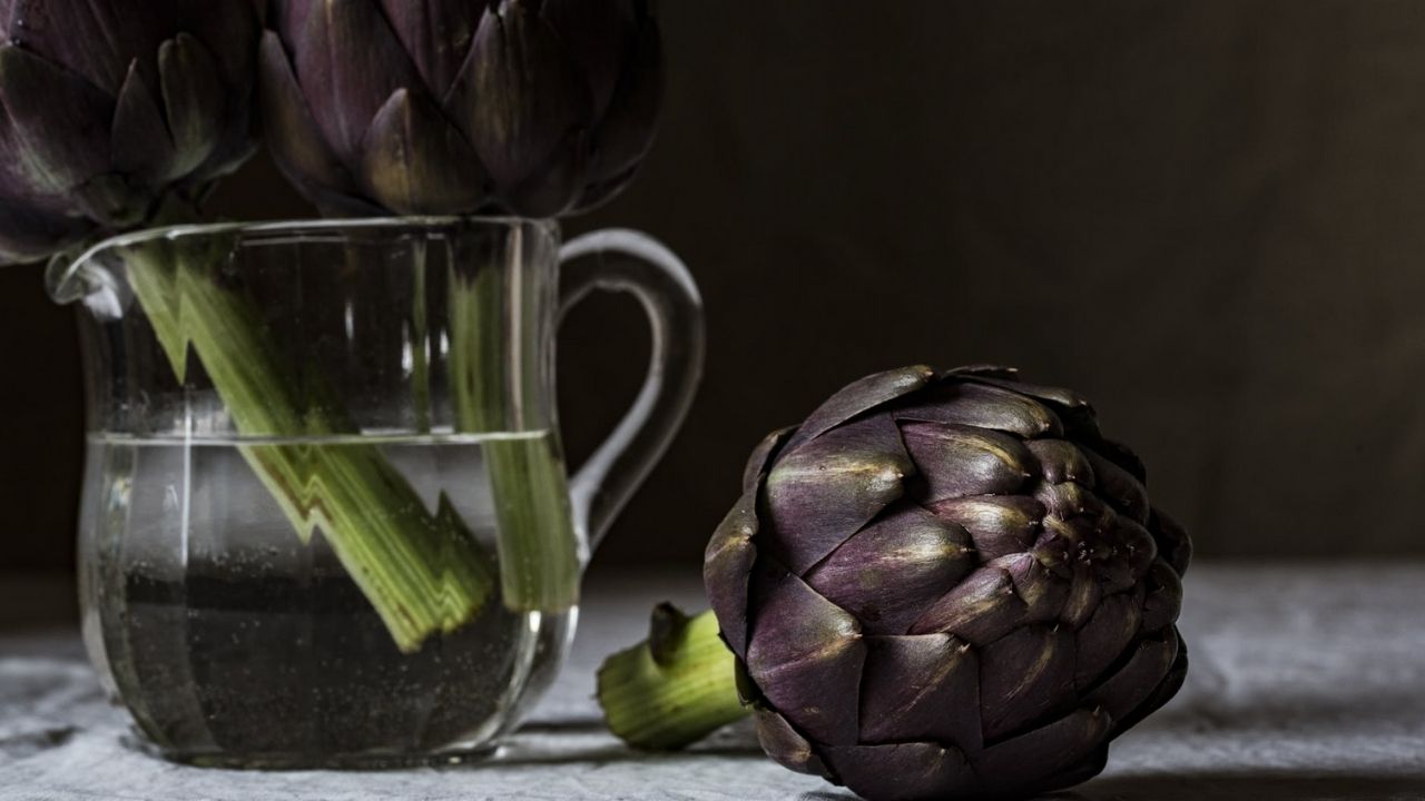 carciofo sul tavolo e altri in un vaso con acqua